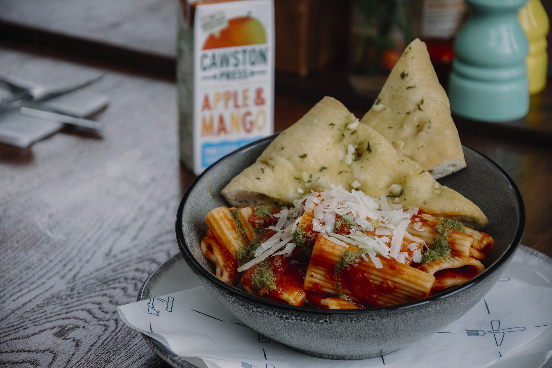 A bowl of pasta with tomato sauce, topped with grated cheese and basil, accompanied by triangular bread slices.