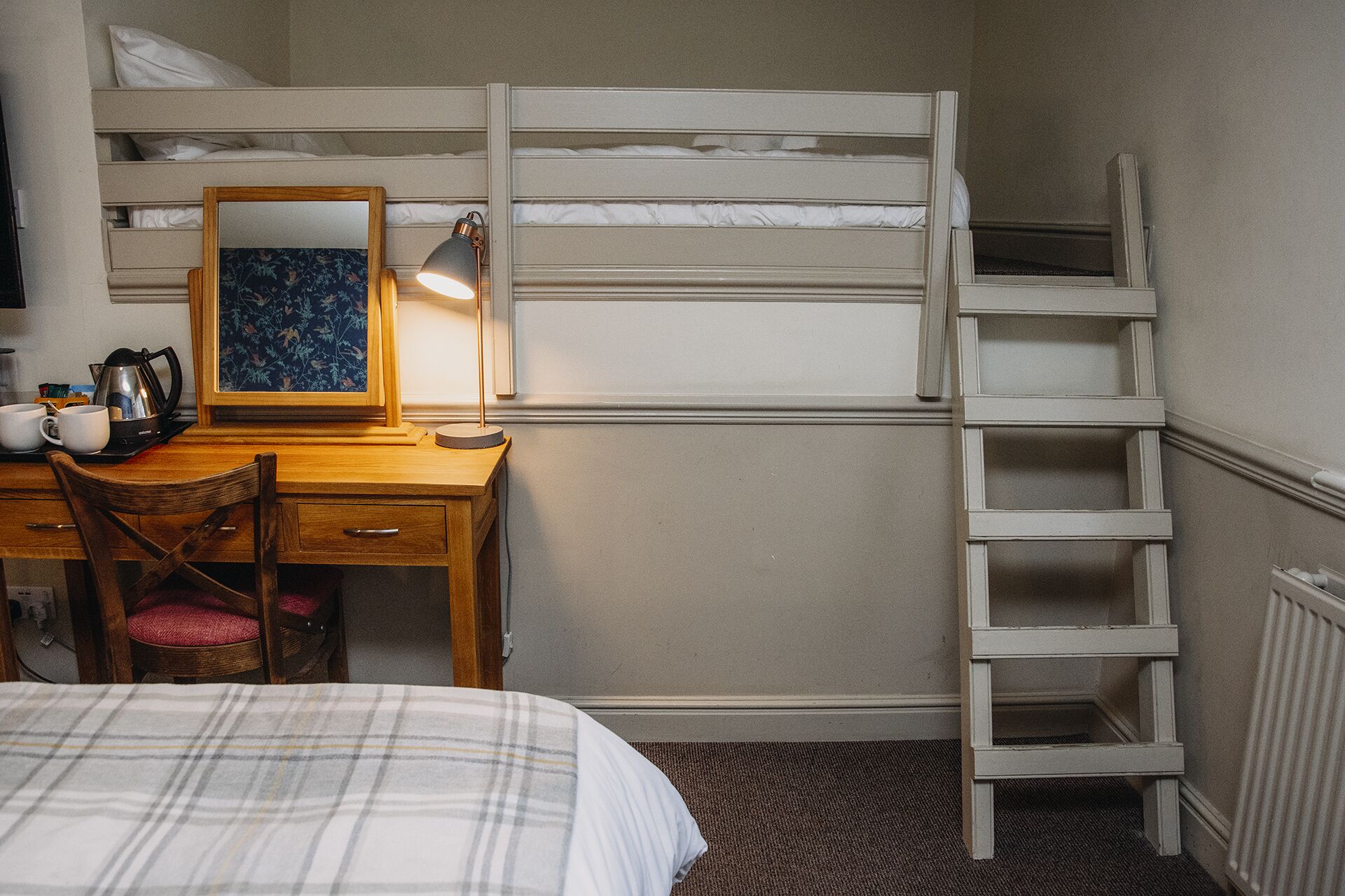 Habitación con literas, escritorio, silla, escalera y un radiador.