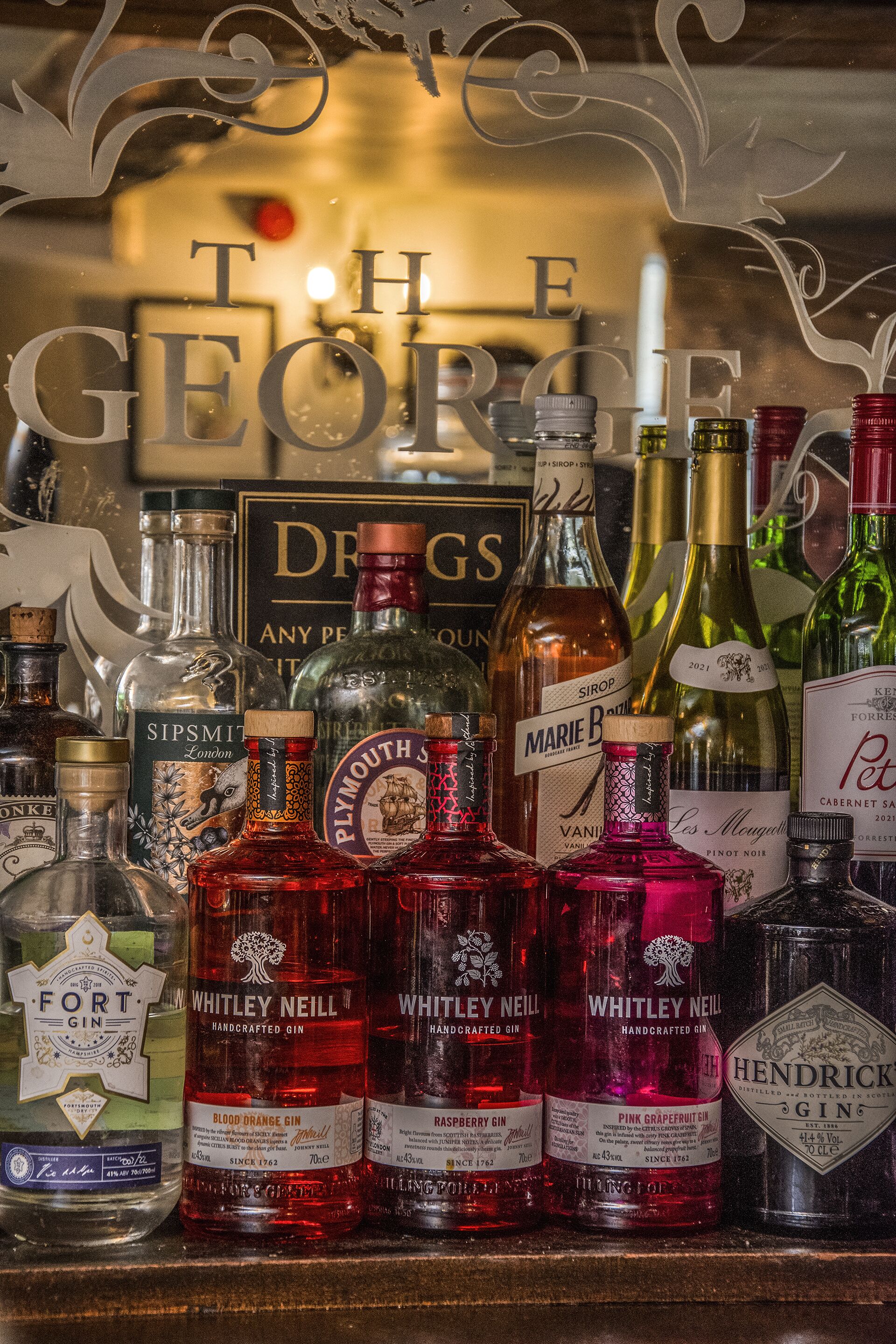 A variety of gin bottles on a shelf with a decorative sign in the background.