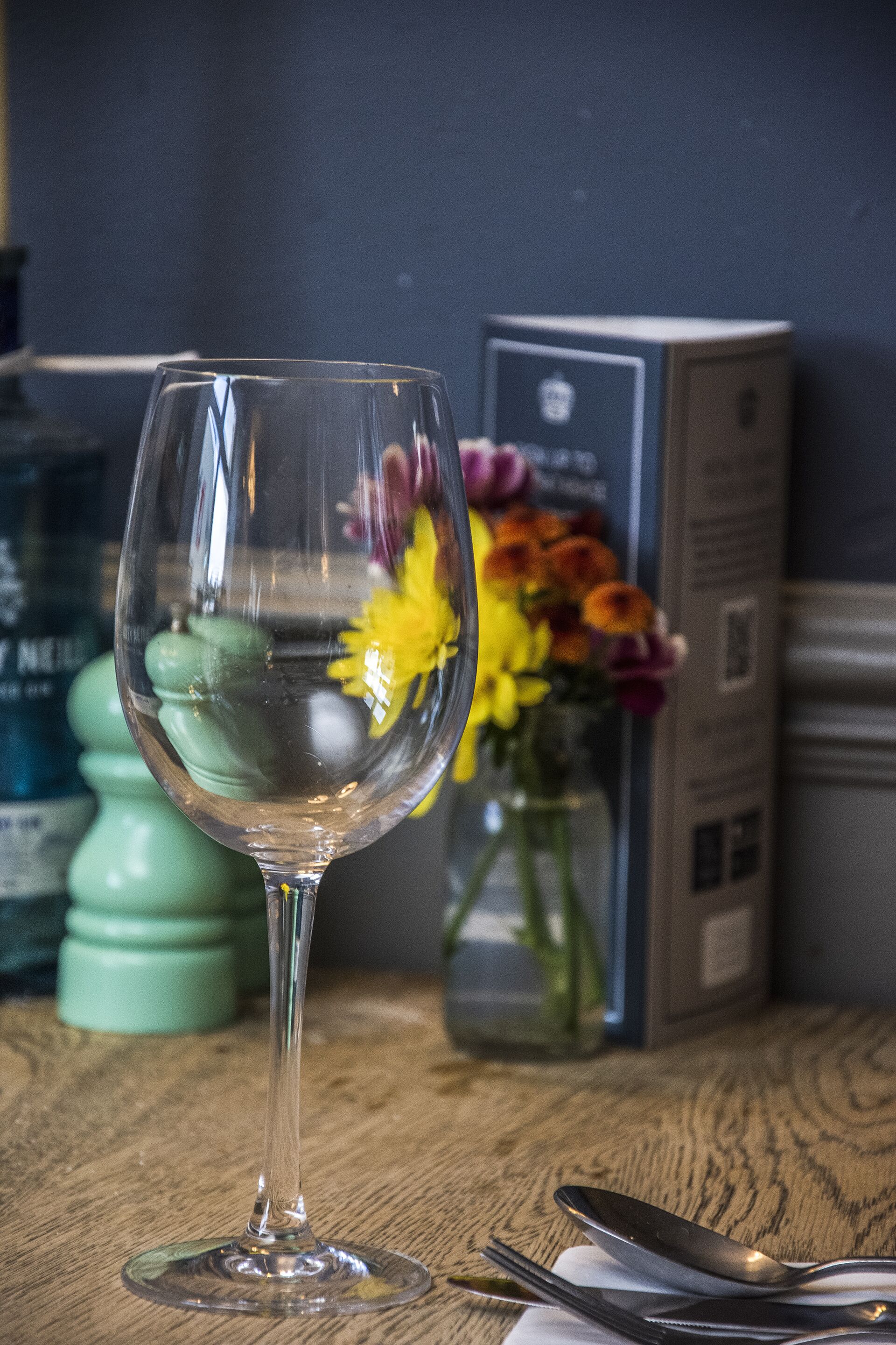 Una copa de vidrio transparente sobre una mesa de madera, con un florero de flores al fondo.
