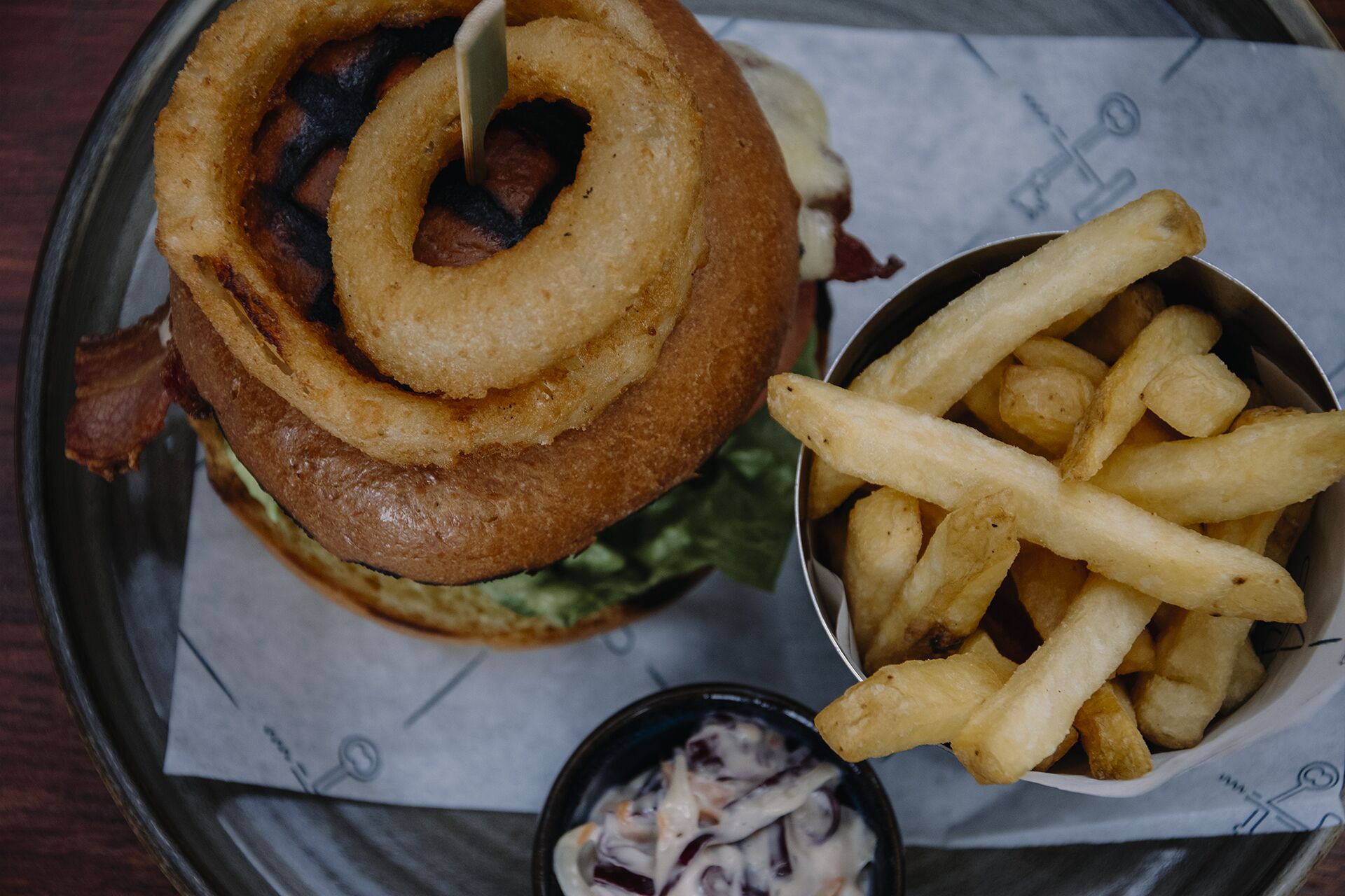 A meal consisting of a burger with onion rings, French fries, and a small bowl of coleslaw.