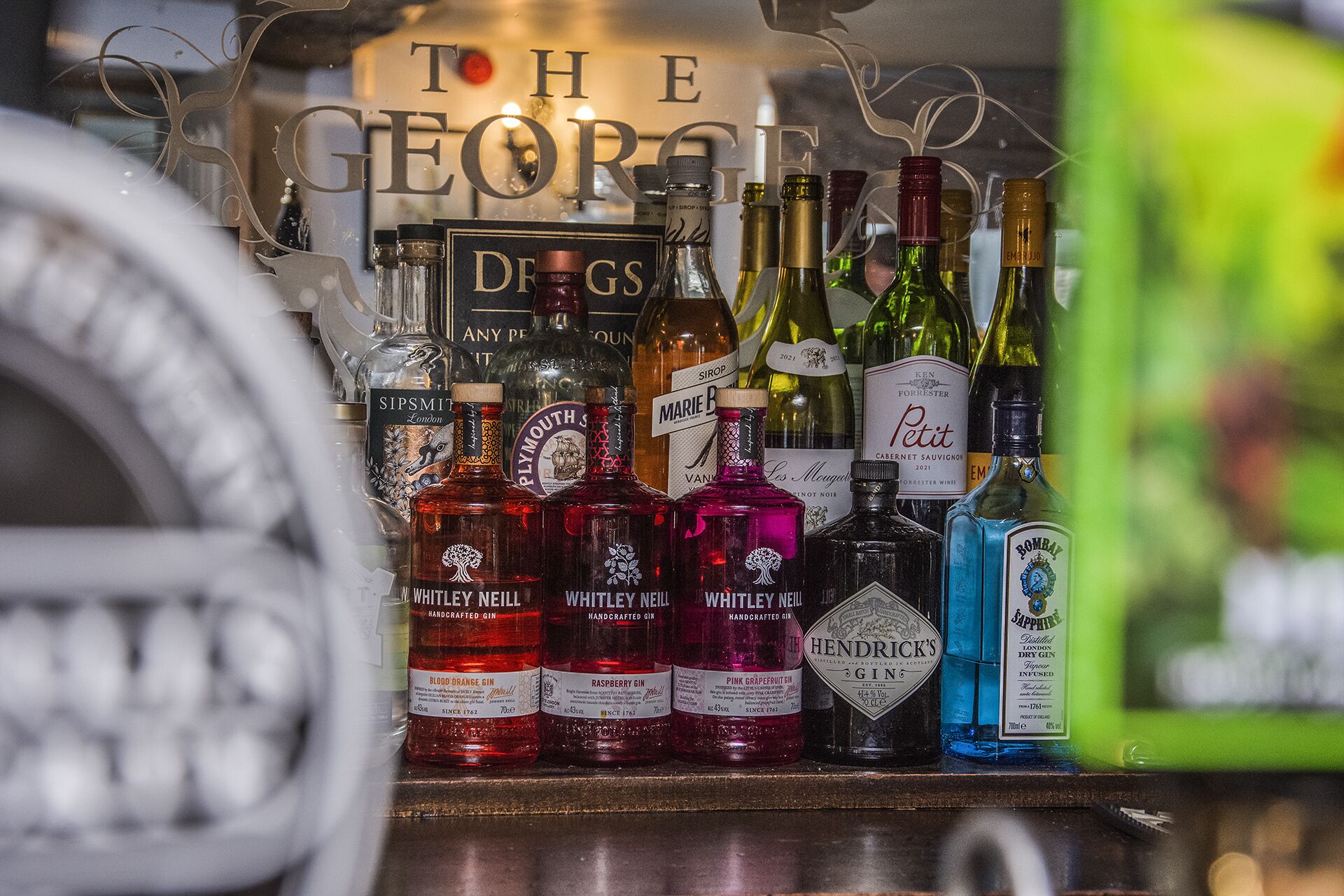 Diverse alcoholflessen op een plank, waaronder gin en wijn.