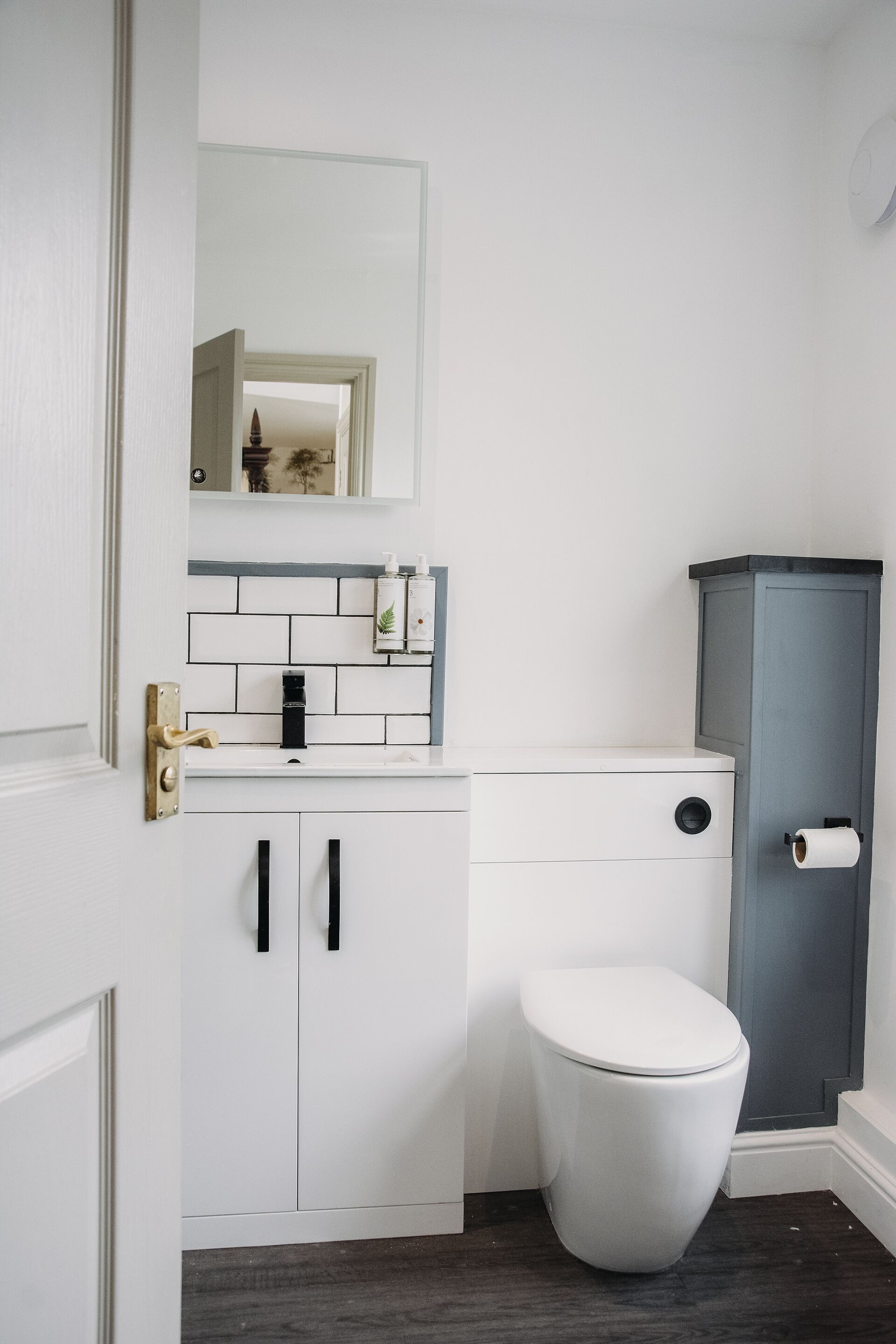 A bathroom with a white toilet, a sink with a mirror above it, and a cabinet with a toilet paper holder.