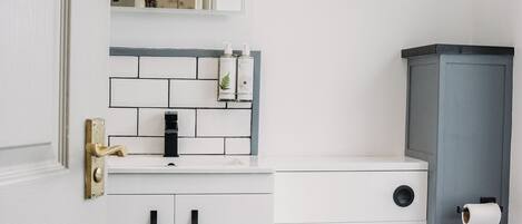 A bathroom with a white toilet, a sink with a mirror above it, and a cabinet with a toilet paper holder.