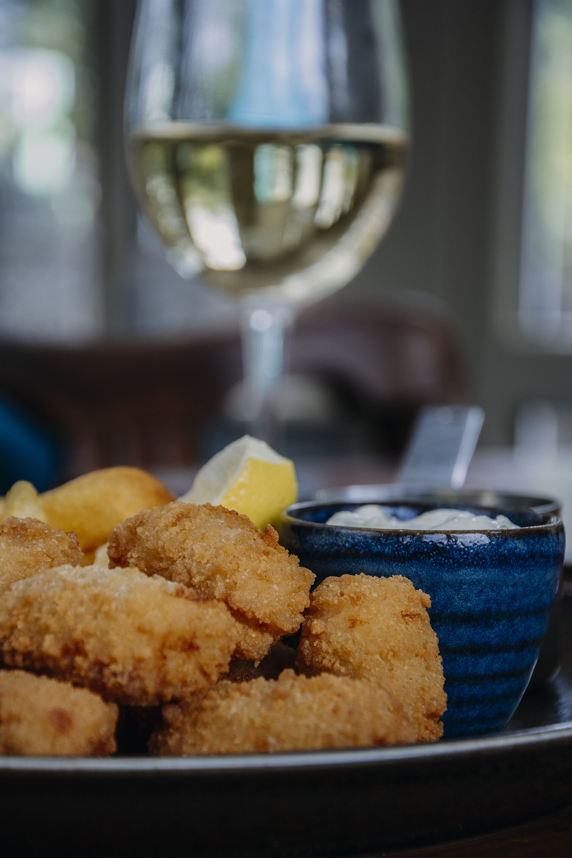 A plate of breaded and fried food, a glass of white wine, and a bowl of dipping sauce.