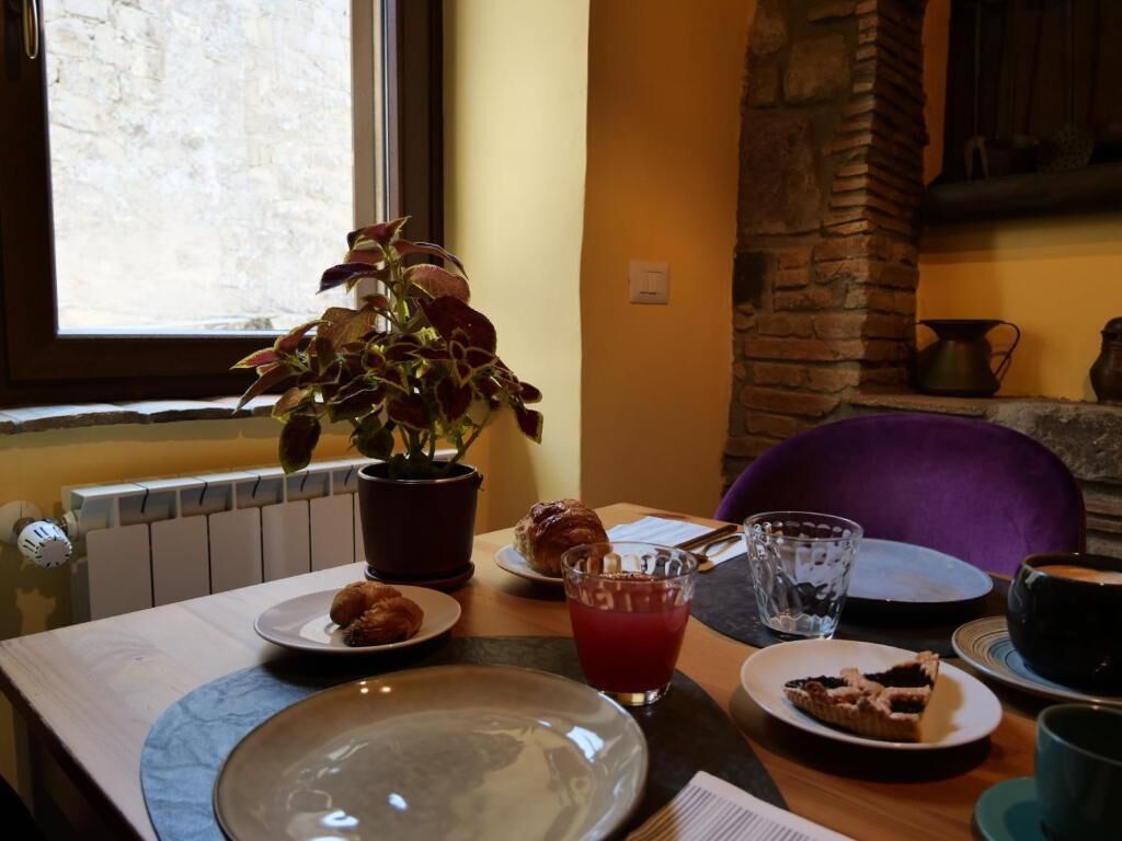 A dining table with plates, a glass of red beverage, a potted plant, and a croissant.