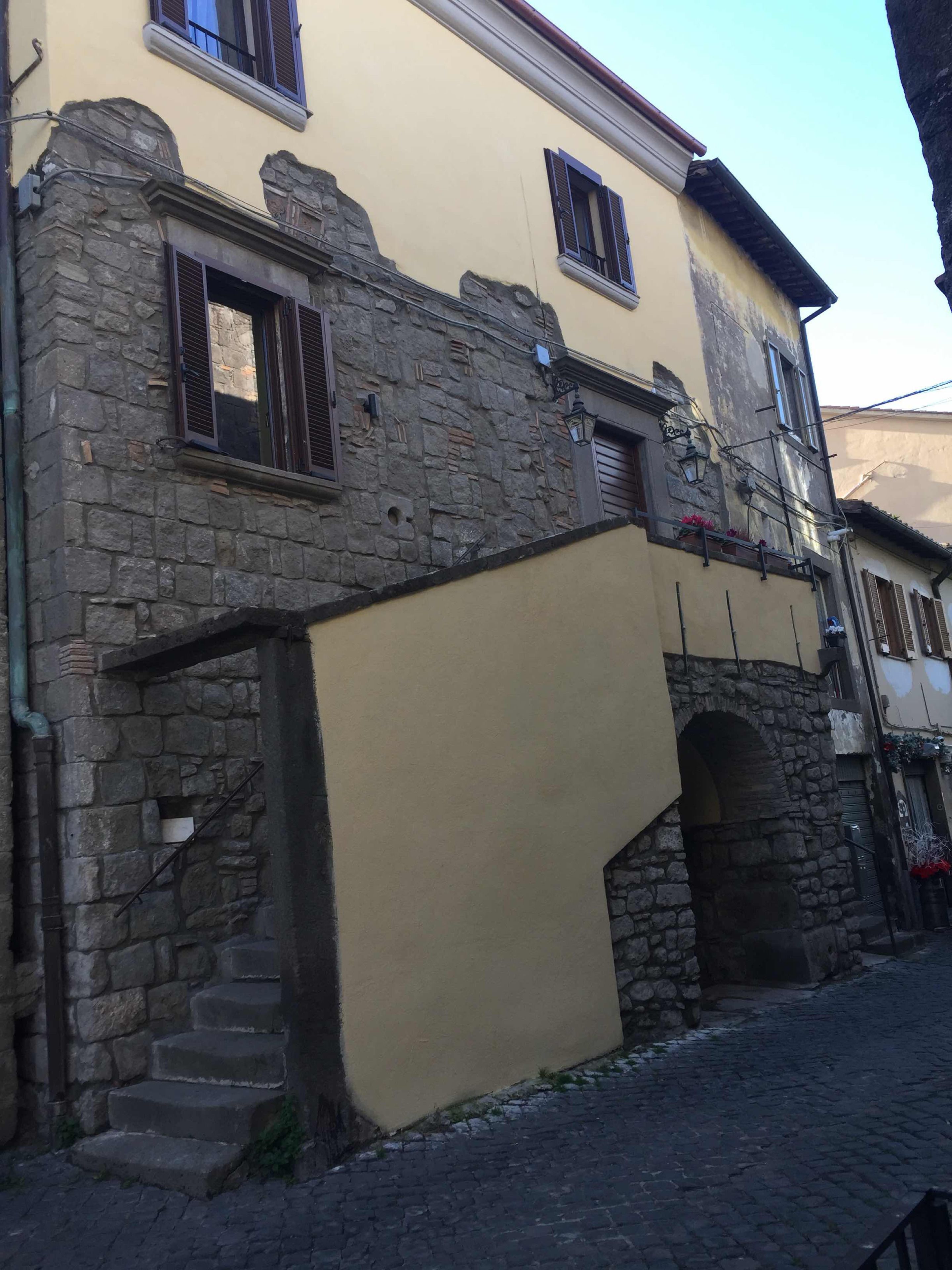 Un edificio con fachada de piedra, un nivel superior amarillo y una calle empedrada.