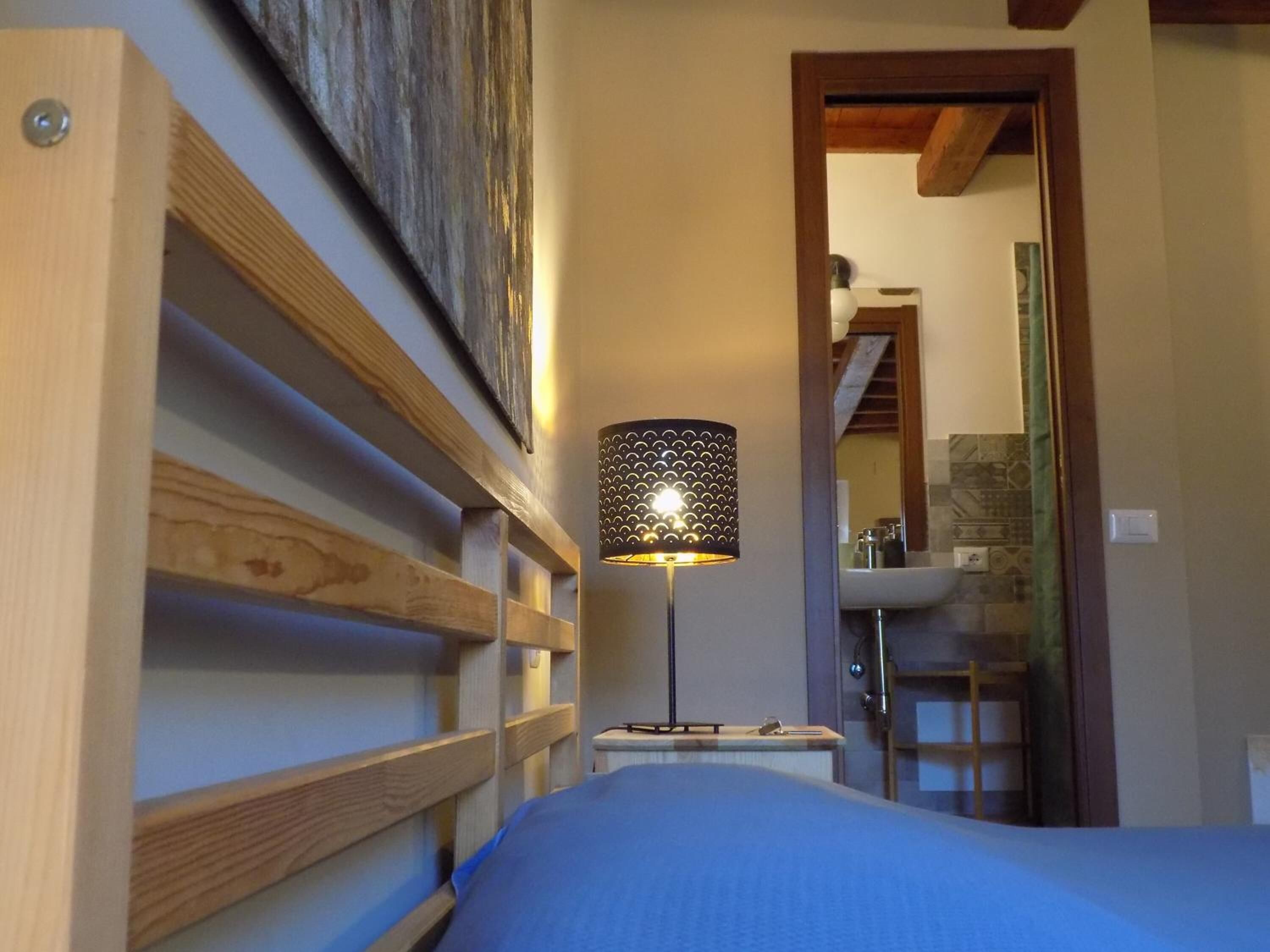 A bedroom with a wooden headboard, a bedside lamp, and a view of a bathroom with a sink and mirror.