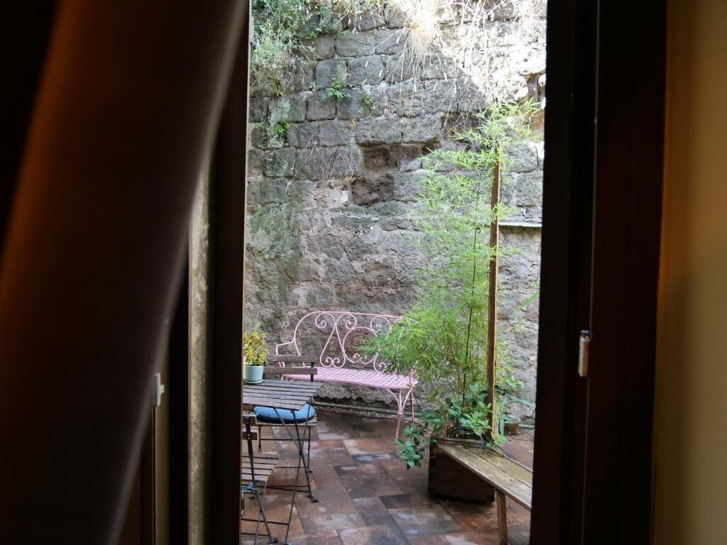 A stone wall, a metal bench, and a table with chairs in an outdoor area.