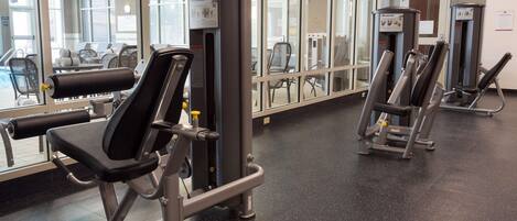 Une salle de sport équipée de machines d’exercice, dotée de grandes fenêtres et d’un sol à motifs.