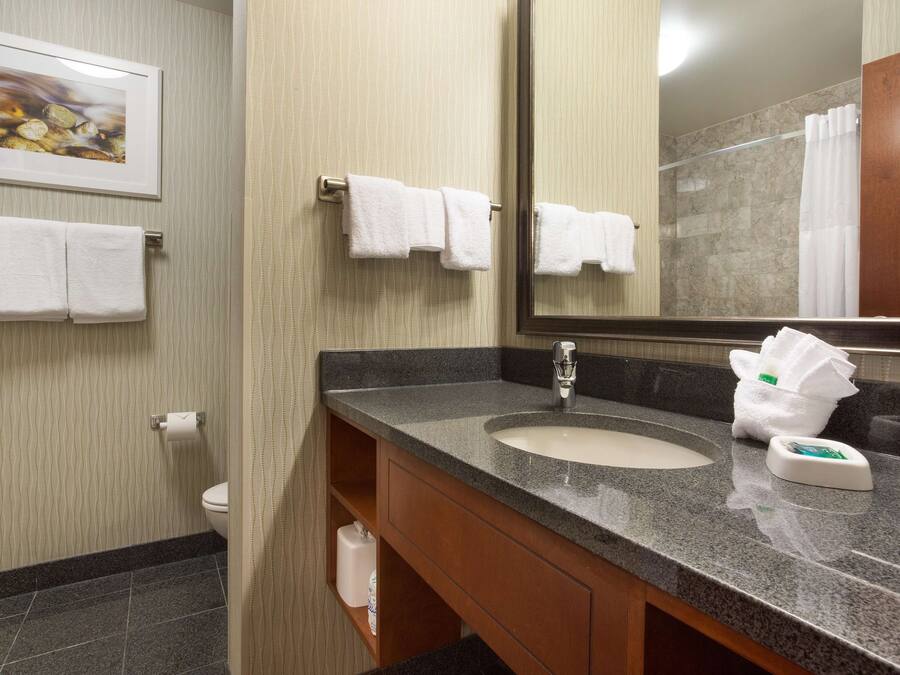 A bathroom with a sink, mirror, towels, and a toilet.