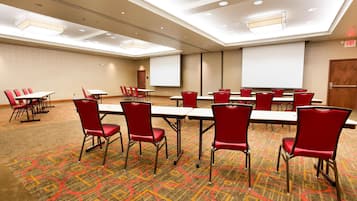 A conference room with red chairs and tables, a projector screen, and a carpeted floor.
