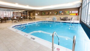 An indoor swimming pool with clear water, surrounded by lounge chairs and tables.