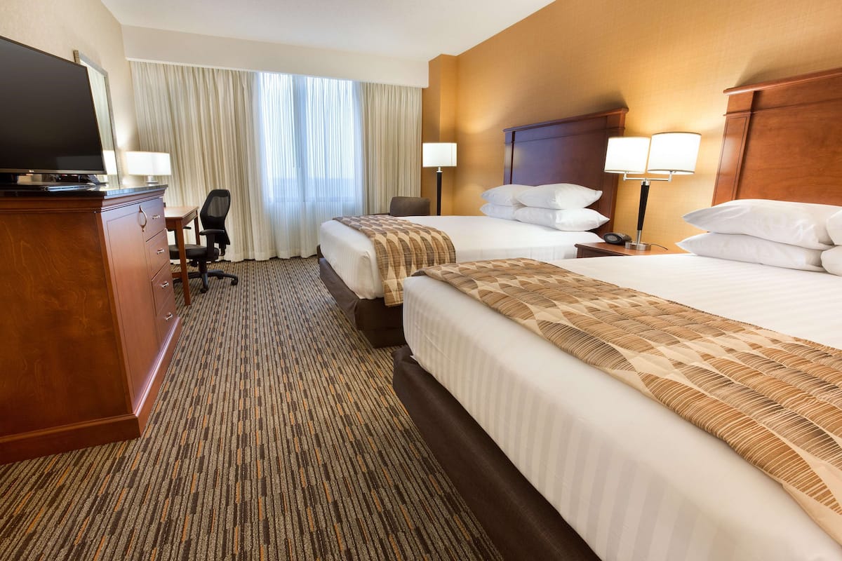 A hotel room with two beds, a desk, a television, and a chair.