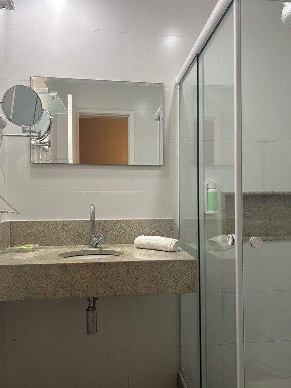 Un baño con encimera de granito, lavamanos, espejo y mampara de vidrio.