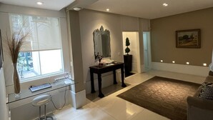 A spacious living room with a large window, a dark wooden coffee table, and a beige sofa.