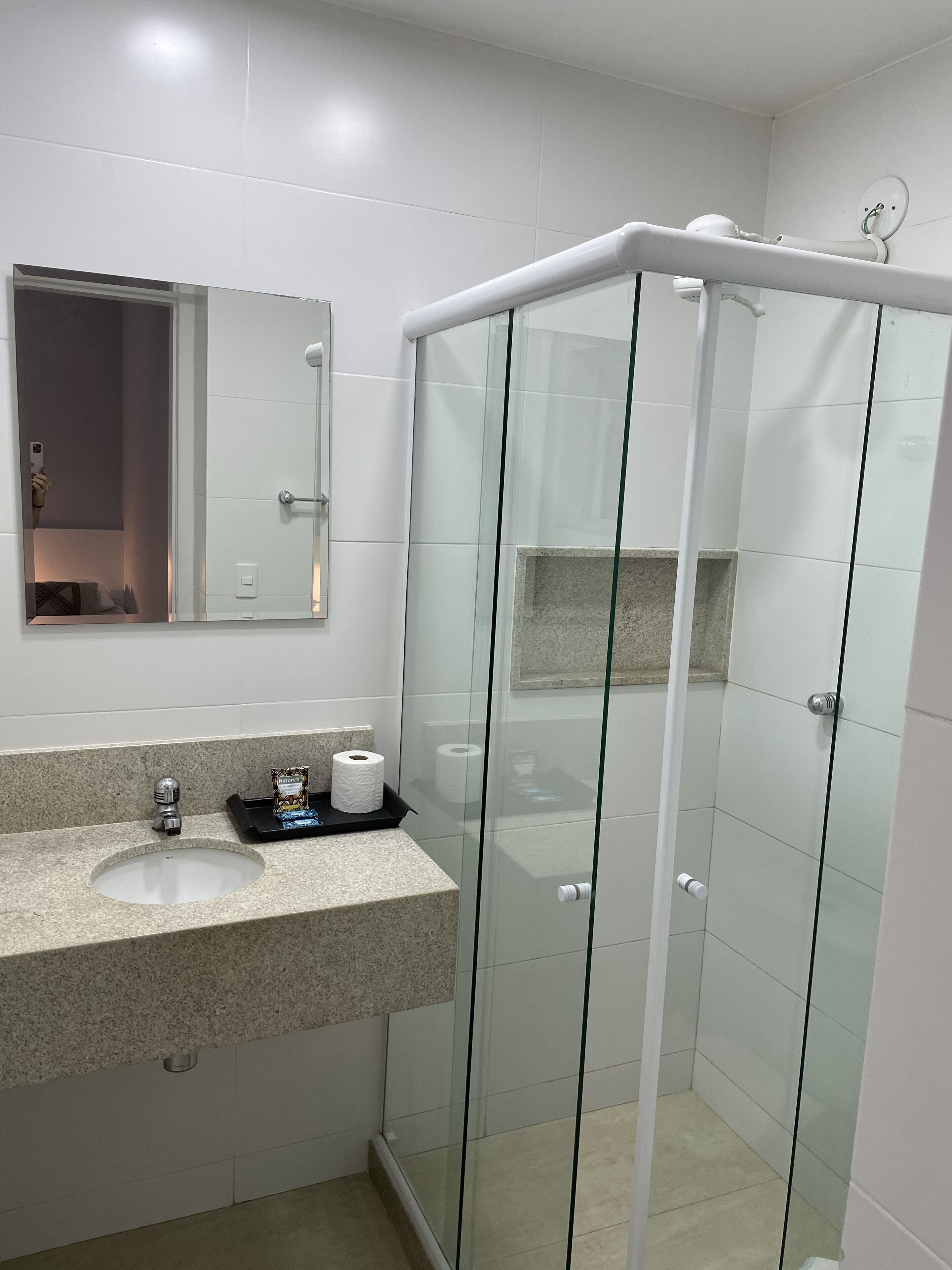 Un baño moderno con ducha envuelta en vidrio, lavabo con encimera de granito y espejo sobre el lavabo.