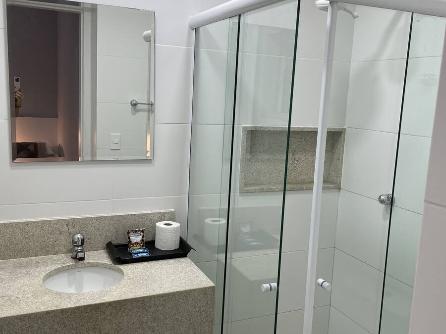 Un baño moderno con ducha envuelta en vidrio, lavabo con encimera de granito y espejo sobre el lavabo.