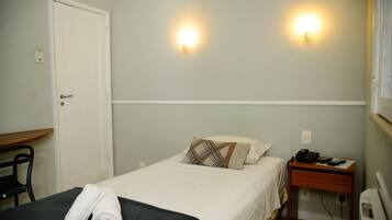 A hotel room with a bed, a desk, and two wall-mounted lights.