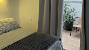 A bedroom with a bed, a potted plant, and a view of the outside.