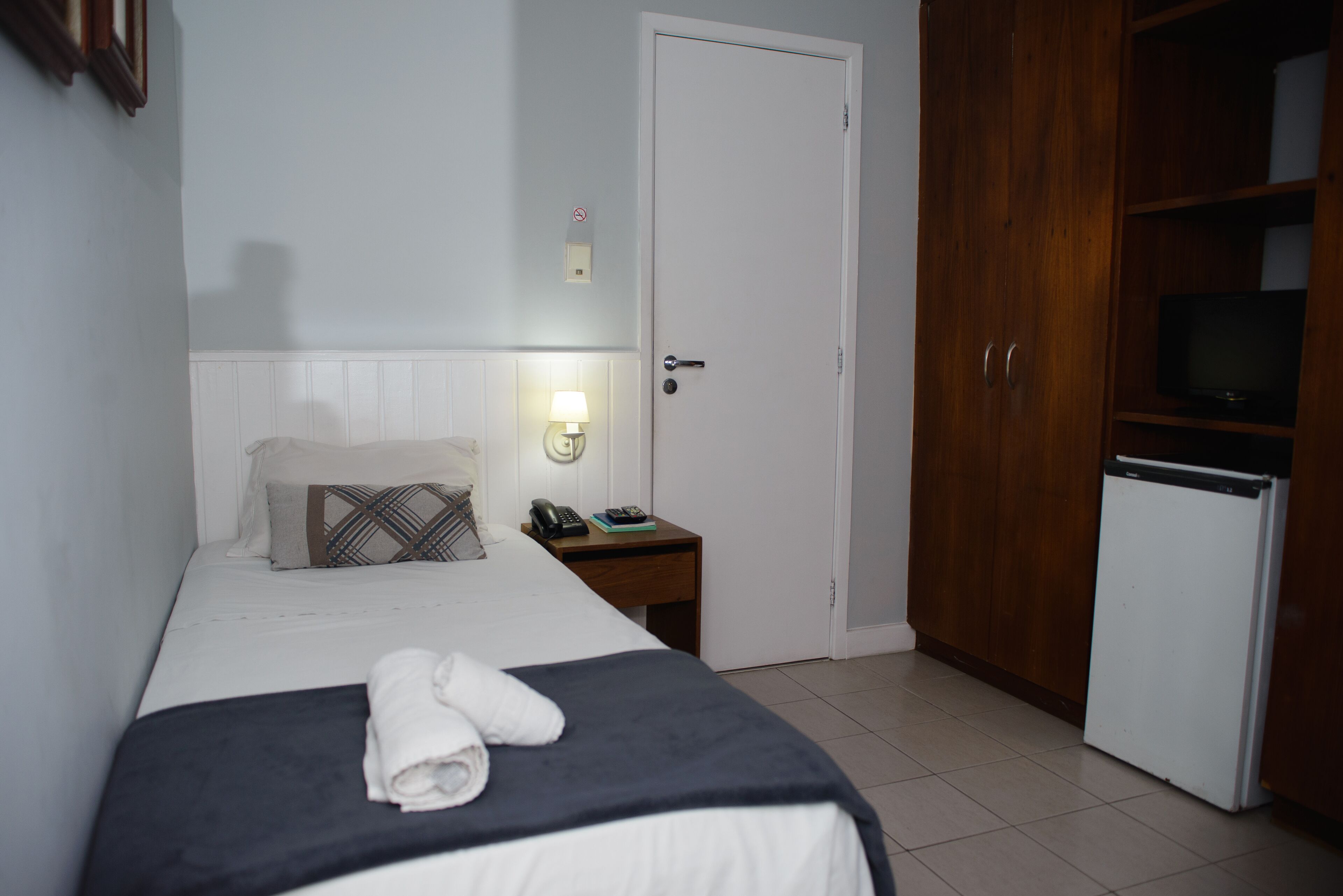 Hotelkamer met een bed, nachtkastje met lamp, telefoon en televisie op een kast.