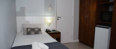 A hotel room with a bed, a bedside table with a lamp, a telephone, and a television on a cabinet.