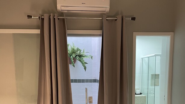 A hotel room with a bed, a chair, an air conditioning unit, and a view of the outside.