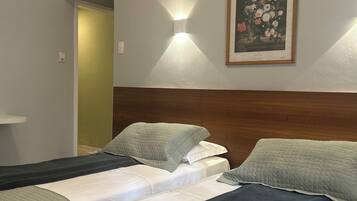 A hotel room with two beds, a wooden headboard, a framed floral artwork, and a wall-mounted light fixture.