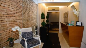 A reception area with a brick wall, a reception desk, a seating area with patterned chairs, and potted plants.