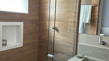 A modern bathroom with a glass shower enclosure, a vanity with a granite countertop, and a wooden wall.