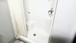 A white shower enclosure with a drain, a shower control knob, and a curtain.