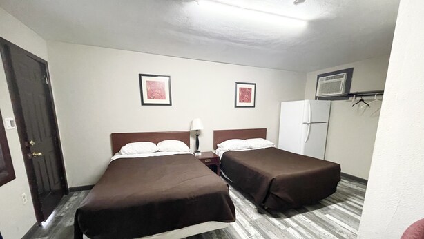 A hotel room with two beds, a refrigerator, a wardrobe, and a door.