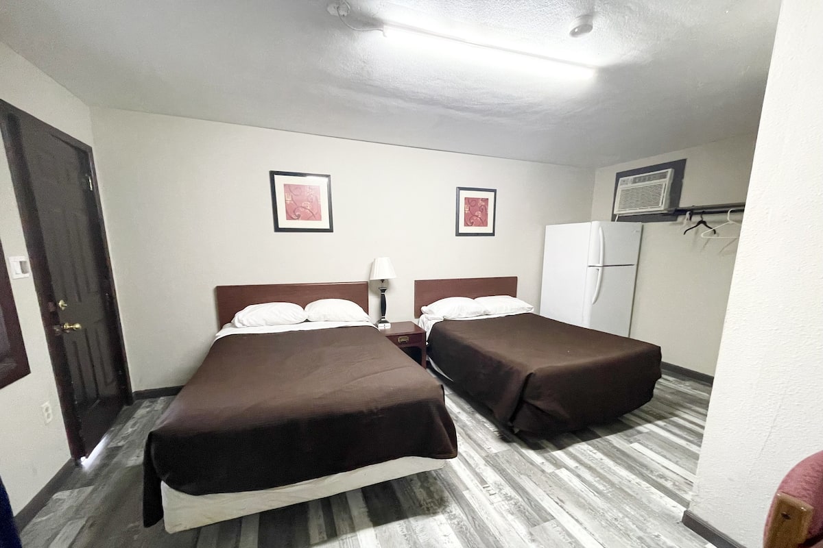 Habitación de hotel con dos camas, un refrigerador, un armario y una puerta.