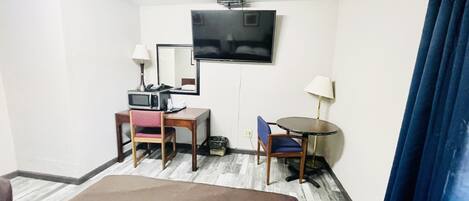 Quarto de hotel com cama, escrivaninha, computador, cadeira, mesinha, televisão e espelho.