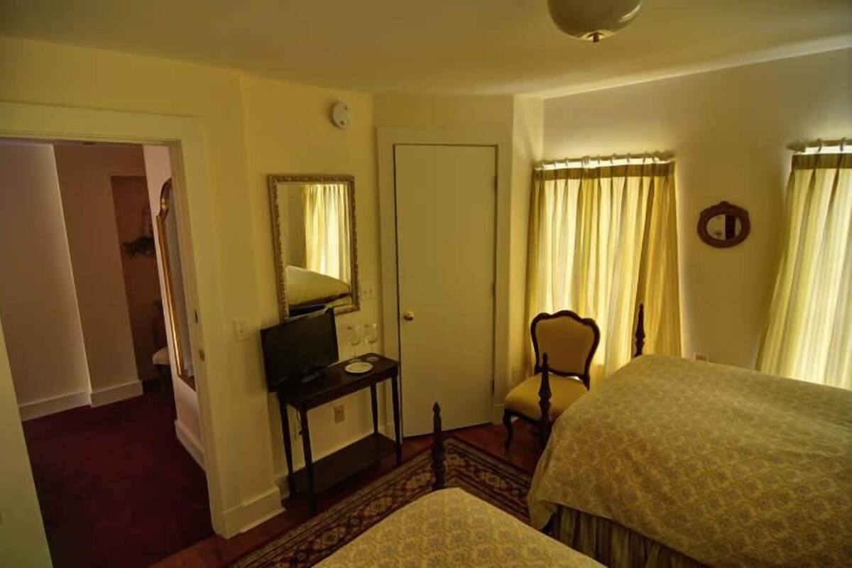 A hotel room with a bed, a desk with a computer, a chair, a mirror, and a door.
