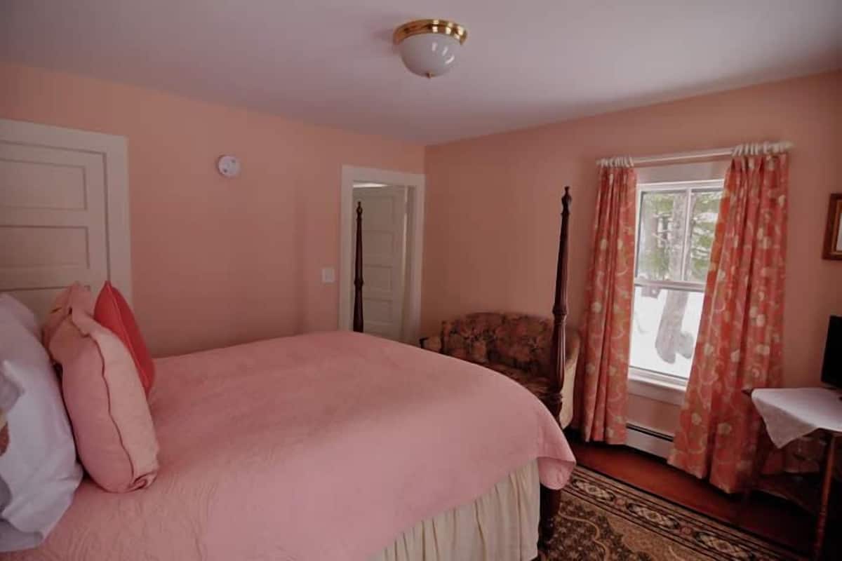 A bedroom with a bed, a chair, a window with curtains, and a door.