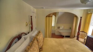 Un dormitorio con una cama grande, cabecera de madera y baño visible a través de un arco.