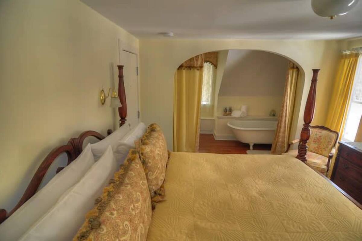 A bedroom with a large bed, a wooden headboard, and a bathroom visible through an arched doorway.