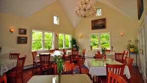 Comedor con sillas de madera, una mesa de vidrio y una araña. Se ven plantas a través de las ventanas.