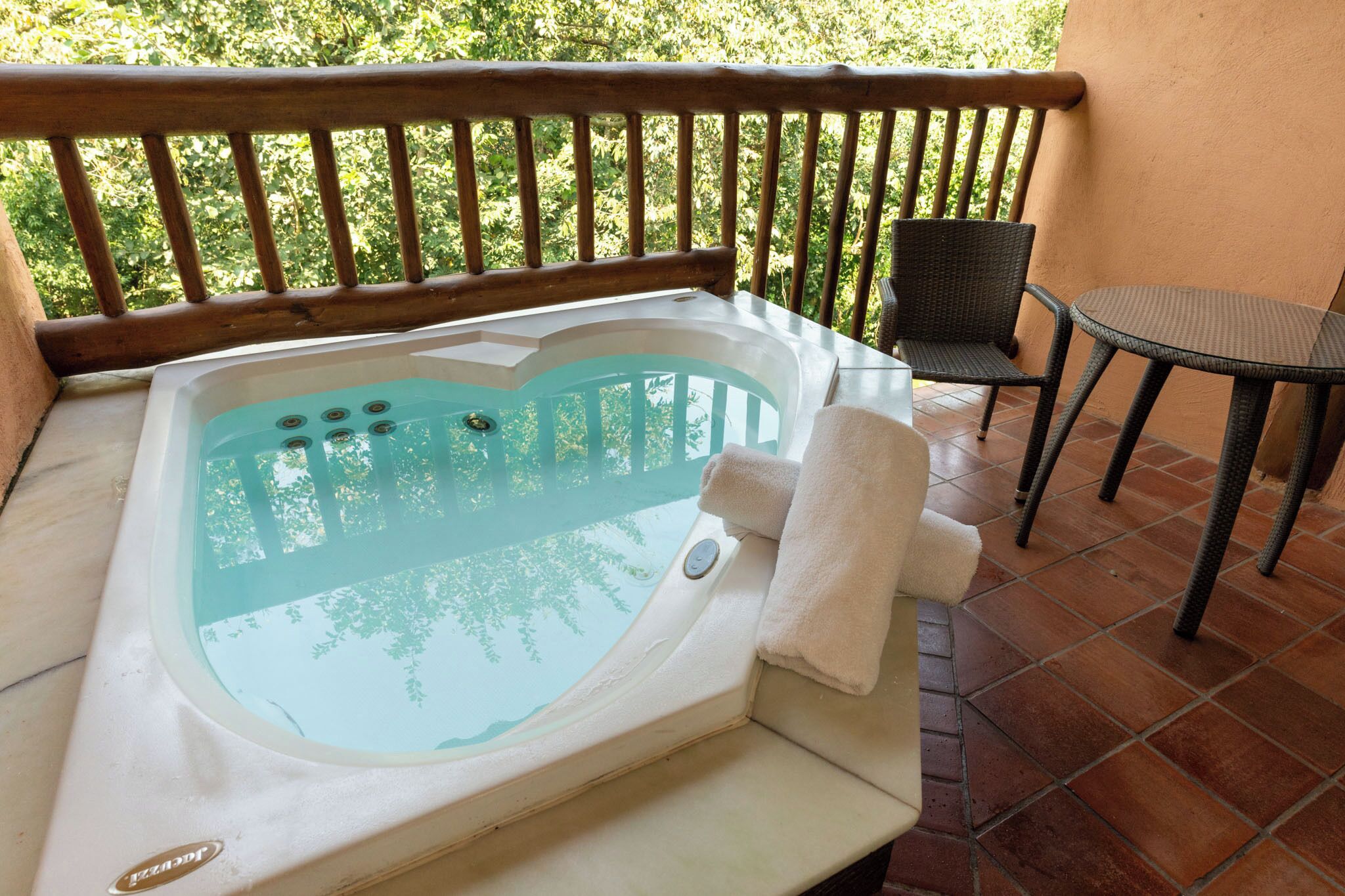 Un jacuzzi en un balcón con barandilla de madera, una mesa y sillas.