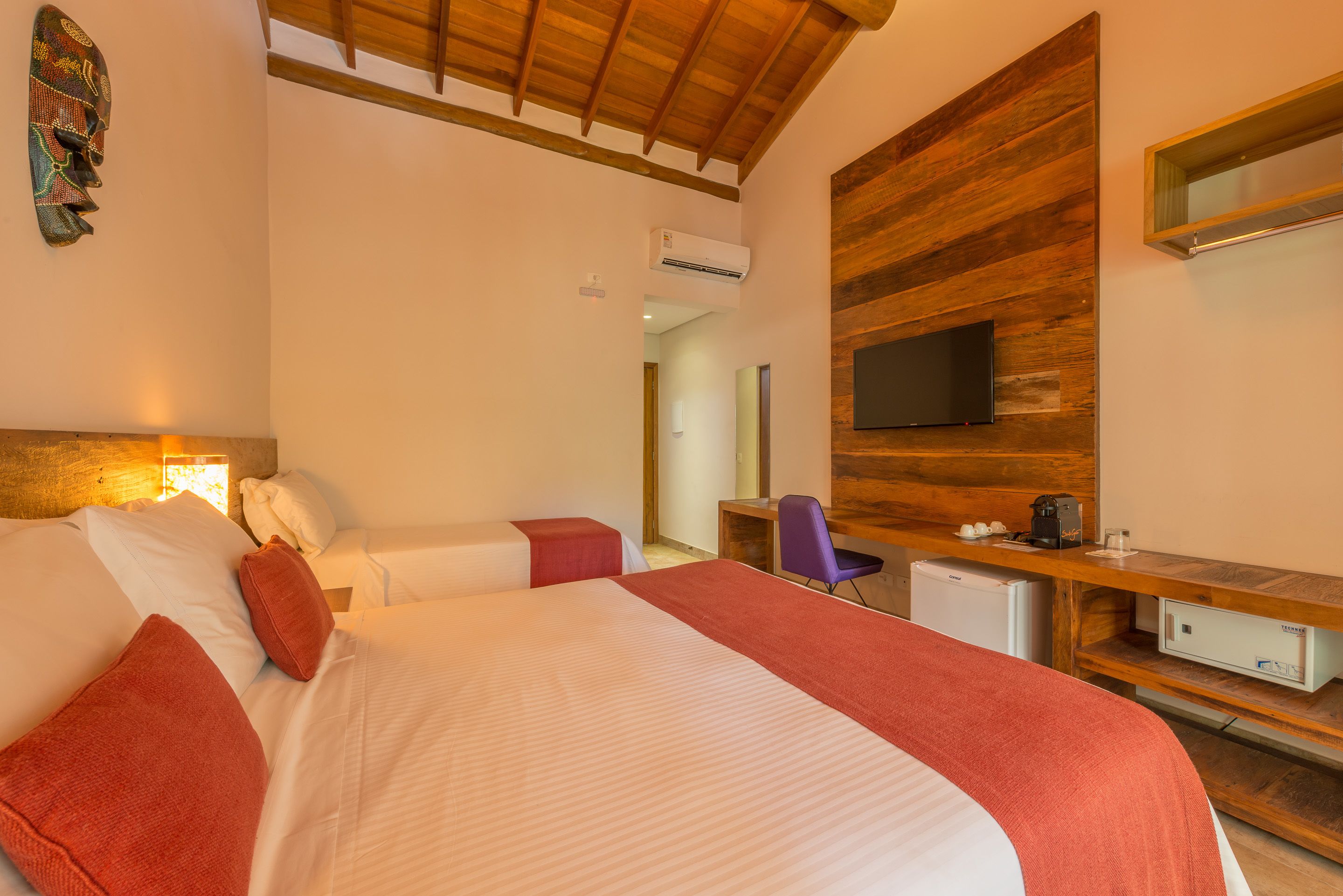 Habitación de hotel con una cama grande, un escritorio con computadora, un televisor y un refrigerador pequeño.