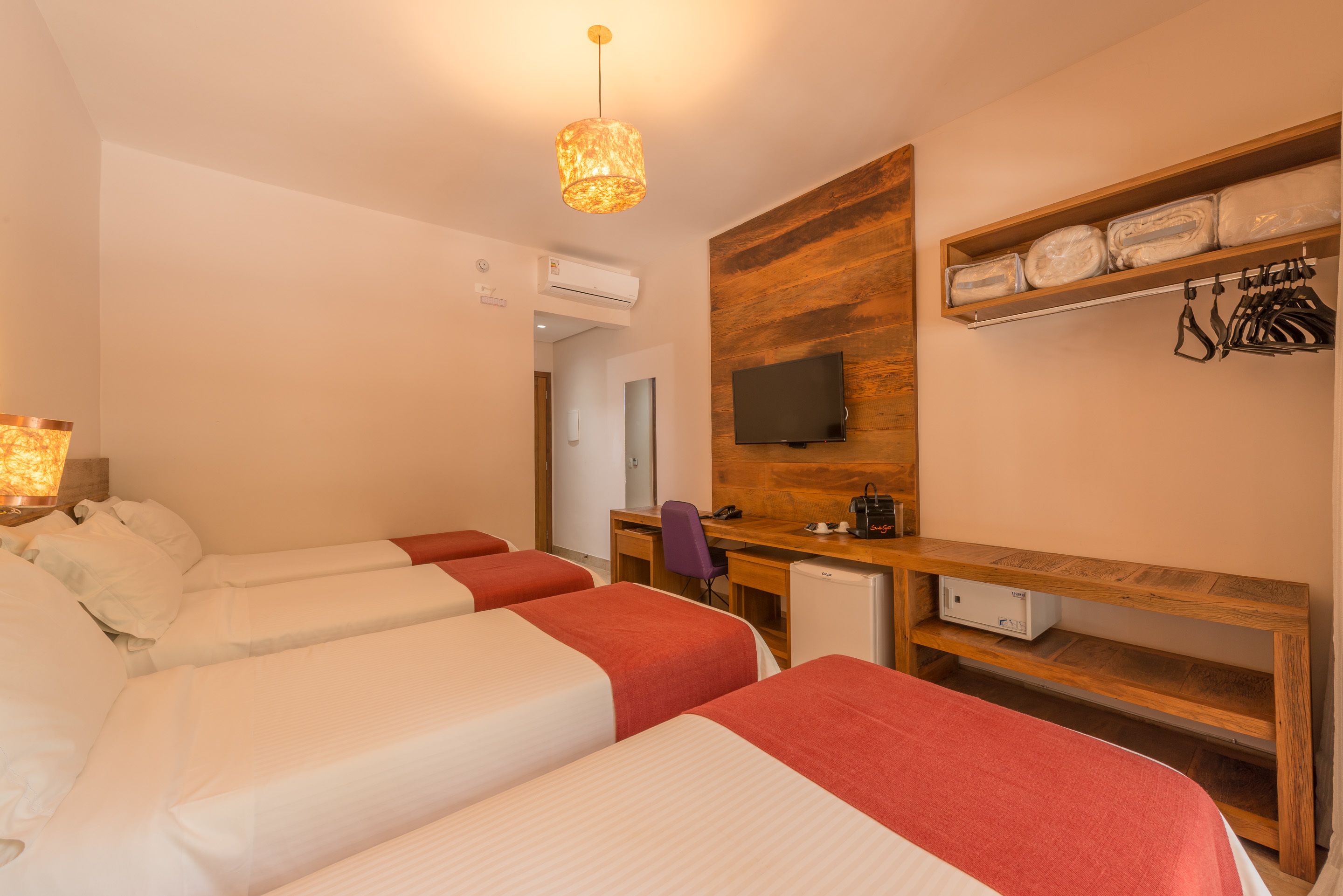 Habitación de hotel con dos camas, un escritorio, una silla, un televisor y una repisa con toallas dobladas y una bolsa.