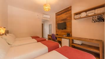 Habitación de hotel con dos camas, un escritorio, una silla, un televisor y una repisa con toallas dobladas y una bolsa.