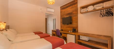 A hotel room with two beds, a desk, a chair, a television, and a shelf with folded towels and a bag.