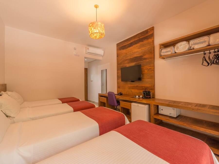 Habitación de hotel con dos camas, un escritorio, una silla, un televisor y una repisa con toallas dobladas y una bolsa.