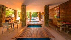Un espace piscine agrémenté d’une terrasse en bois, de piliers en pierre et de mobilier en osier.