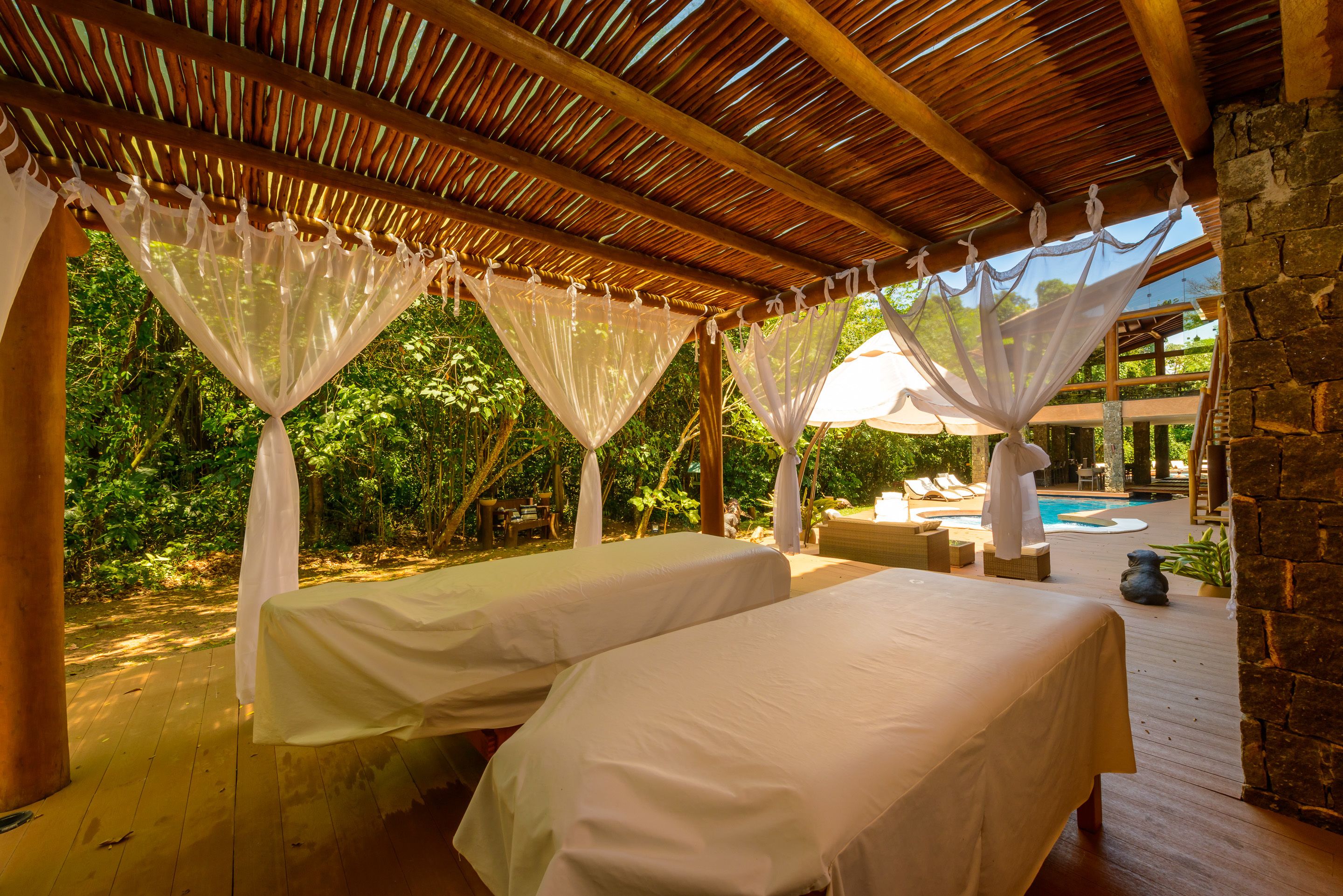A covered outdoor area with two beds, a pool, and a stone wall.