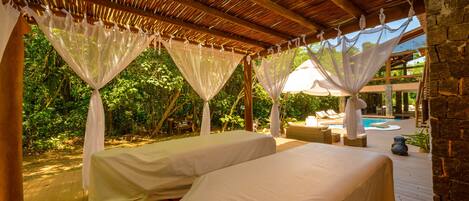 A covered outdoor area with two beds, a pool, and a stone wall.