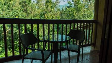 Varanda com duas cadeiras de vime e uma mesa de vidro, com vista para uma paisagem verde exuberante.
