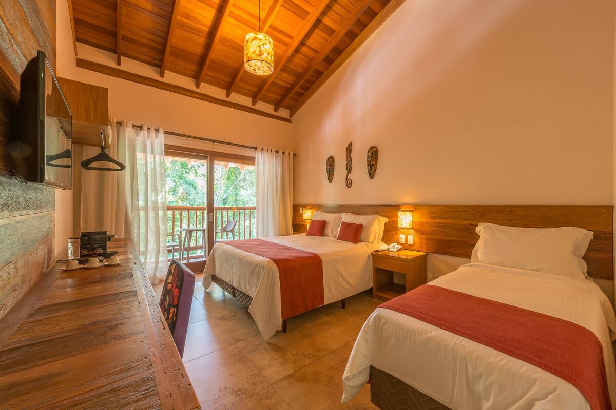 A hotel room with two beds, wooden flooring, a balcony, and a TV mounted on the wall.